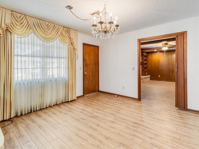 empty room with a textured ceiling, ceiling fan with notable chandelier, and light wood-type flooring