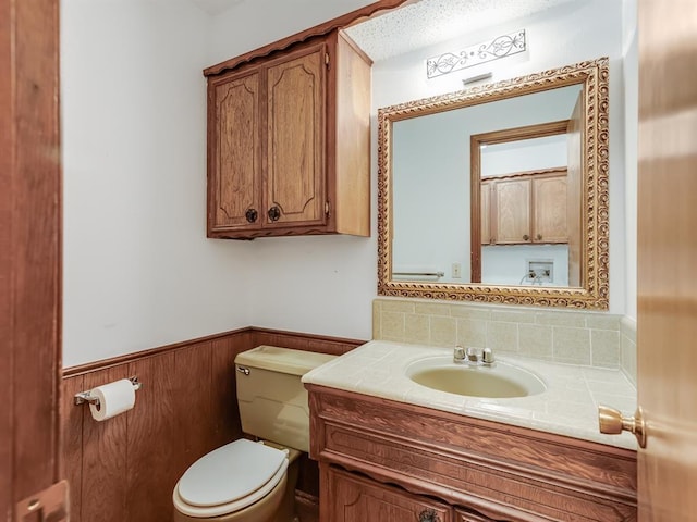 bathroom featuring toilet, wooden walls, and vanity