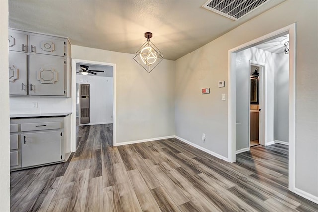 unfurnished dining area featuring ceiling fan with notable chandelier and hardwood / wood-style floors