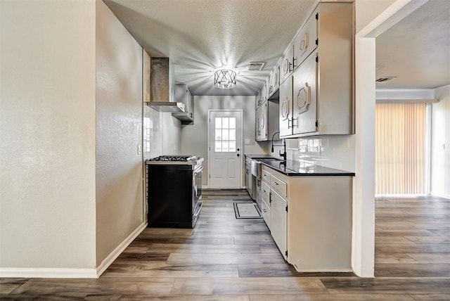 kitchen featuring dark wood-type flooring, stainless steel gas range, tasteful backsplash, and wall chimney range hood