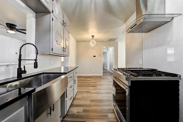 kitchen featuring ceiling fan, extractor fan, stainless steel gas range oven, light wood-type flooring, and white cabinets