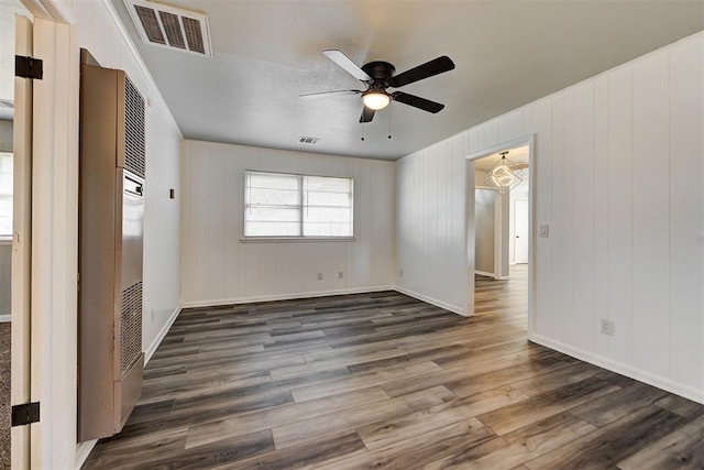 empty room featuring ceiling fan with notable chandelier, dark hardwood / wood-style floors, and wooden walls