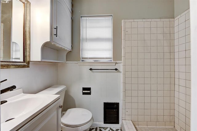 bathroom with toilet, vanity, heating unit, and tiled shower