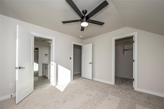 unfurnished bedroom with a spacious closet, ceiling fan, connected bathroom, light colored carpet, and vaulted ceiling