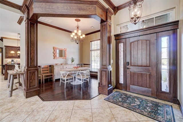 entrance foyer with light tile patterned floors, crown molding, plenty of natural light, a notable chandelier, and ornate columns