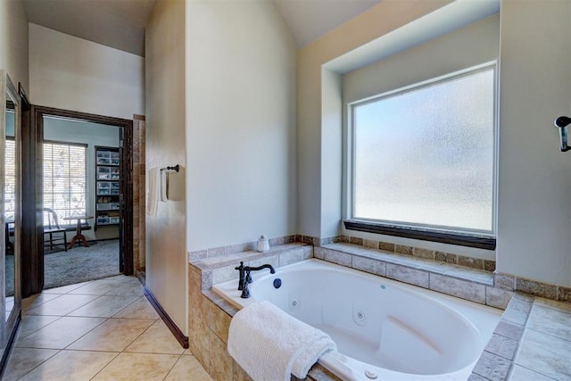 bathroom with tile patterned flooring, vaulted ceiling, tiled bath, and a healthy amount of sunlight