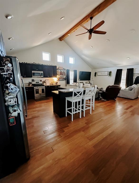 kitchen featuring stainless steel appliances, beamed ceiling, ceiling fan, high vaulted ceiling, and a breakfast bar