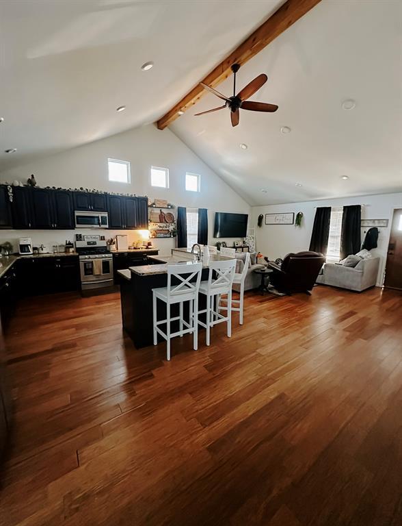 kitchen with appliances with stainless steel finishes, dark hardwood / wood-style floors, ceiling fan, a breakfast bar, and beam ceiling