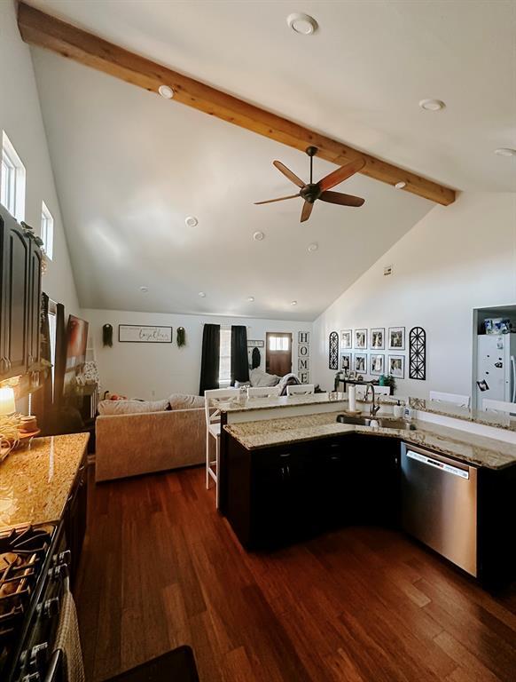 kitchen featuring light stone countertops, range with gas stovetop, dark wood-type flooring, lofted ceiling with beams, and stainless steel dishwasher