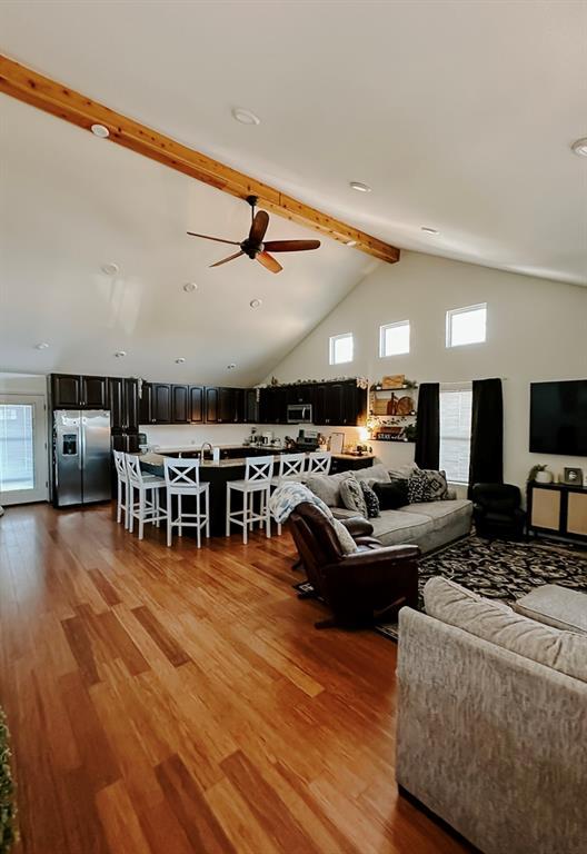 living room featuring ceiling fan, hardwood / wood-style floors, high vaulted ceiling, and beam ceiling