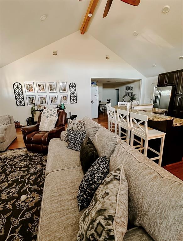 living room featuring ceiling fan, vaulted ceiling with beams, and dark wood-type flooring