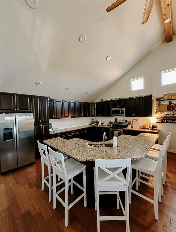 kitchen with stainless steel appliances, light stone counters, a breakfast bar, and high vaulted ceiling