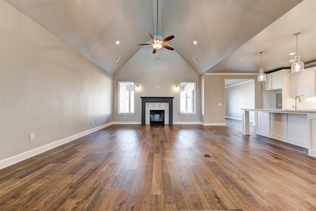 unfurnished living room with lofted ceiling, sink, dark hardwood / wood-style floors, ceiling fan, and a tiled fireplace