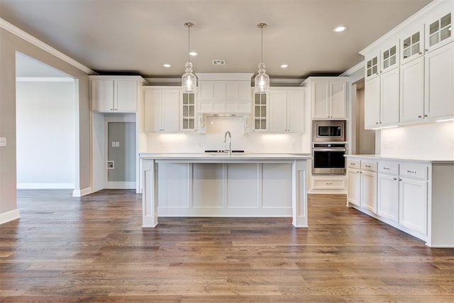 kitchen with a center island with sink, appliances with stainless steel finishes, hanging light fixtures, ornamental molding, and white cabinets