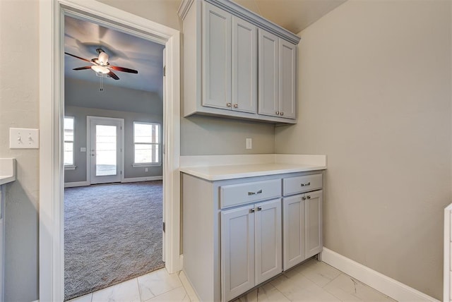 kitchen featuring ceiling fan, light colored carpet, and gray cabinets