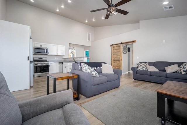 living room with light wood-type flooring, visible vents, a ceiling fan, recessed lighting, and a barn door