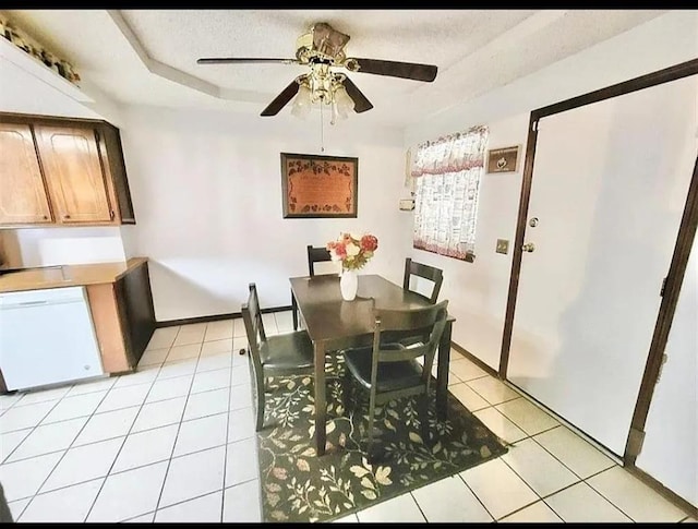 tiled dining space featuring a textured ceiling, ceiling fan, and a tray ceiling