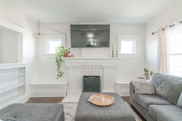 living area featuring a brick fireplace, plenty of natural light, dark wood finished floors, and crown molding