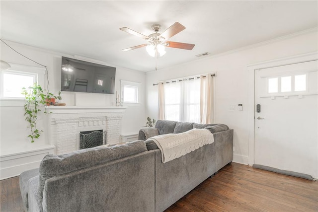 living area with a brick fireplace, crown molding, visible vents, and wood finished floors