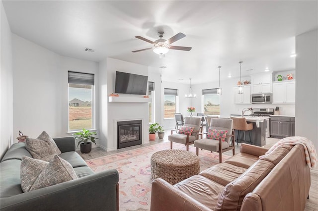 living room featuring light wood-type flooring, a wealth of natural light, and ceiling fan with notable chandelier