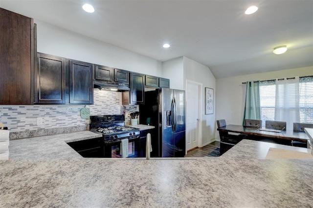 kitchen featuring vaulted ceiling, decorative backsplash, dark brown cabinetry, black appliances, and light stone countertops