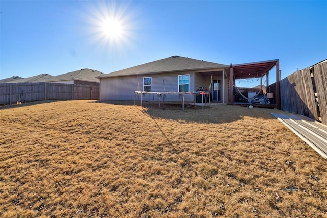 rear view of property featuring a yard and a trampoline