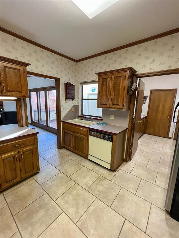 kitchen featuring light countertops, ornamental molding, white dishwasher, a sink, and wallpapered walls