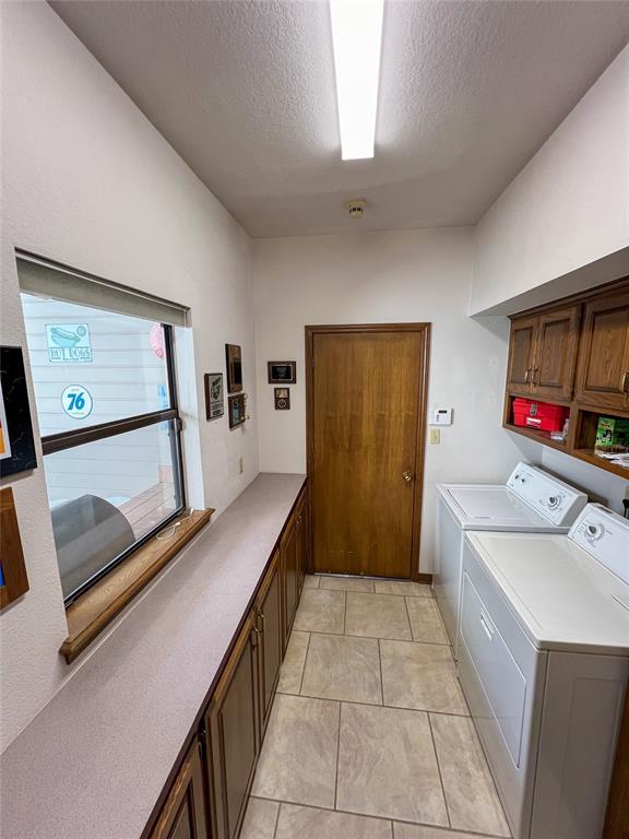 laundry area featuring a textured ceiling, light tile patterned flooring, washing machine and dryer, and cabinet space