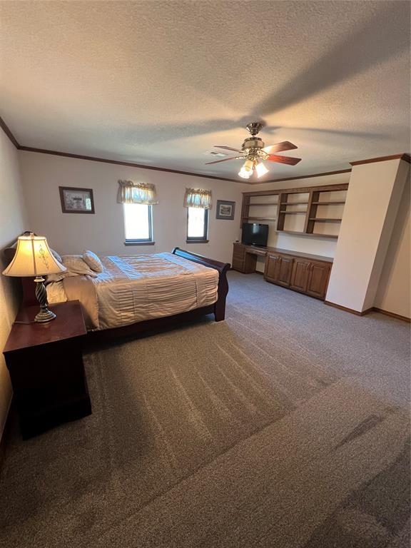 bedroom with a ceiling fan, a textured ceiling, ornamental molding, and carpet flooring