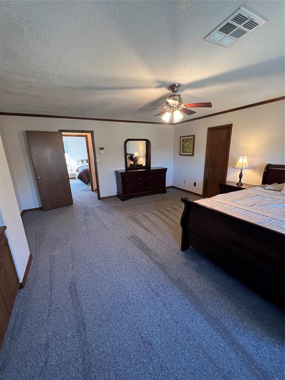 unfurnished bedroom featuring visible vents, crown molding, a textured ceiling, and carpet flooring