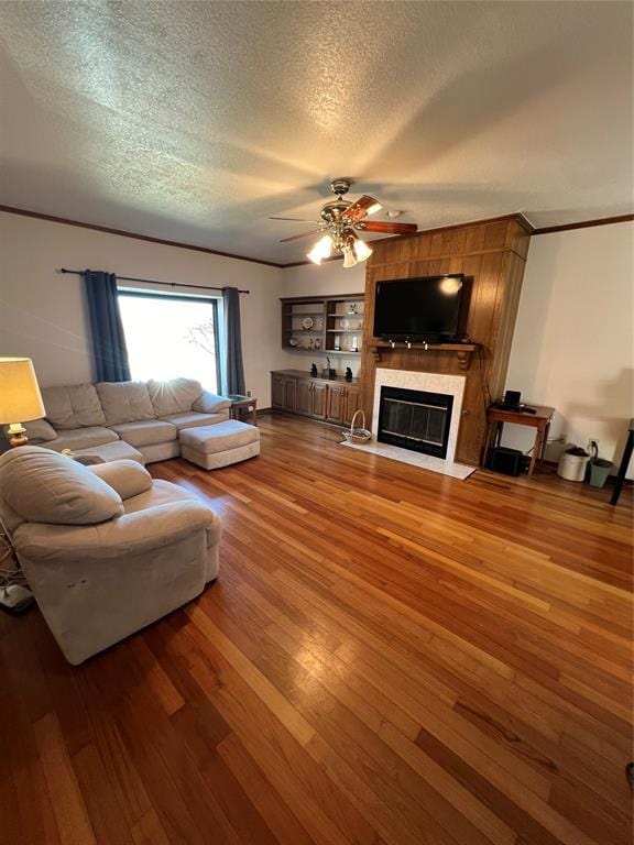 living area with a textured ceiling, ornamental molding, a fireplace, and wood finished floors