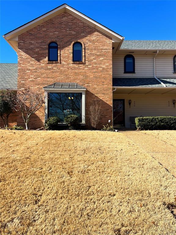 view of front of house featuring a shingled roof, a front yard, and brick siding