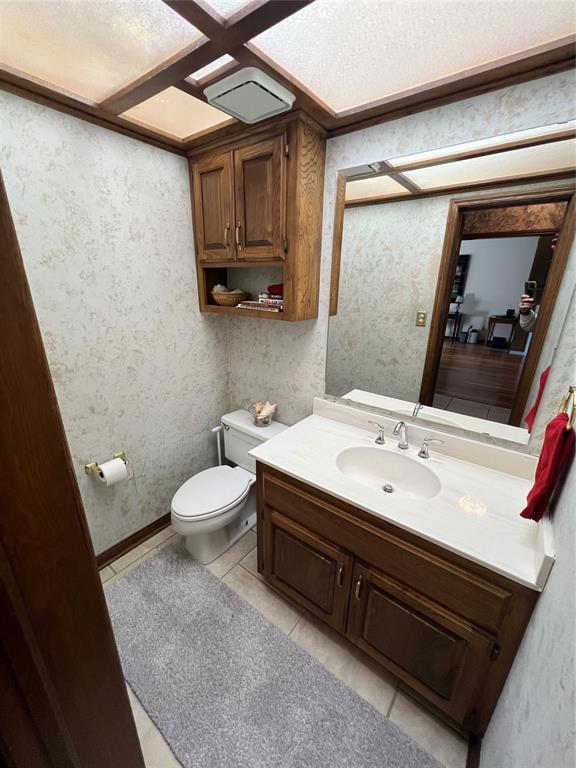 half bathroom featuring tile patterned floors, vanity, toilet, and wallpapered walls