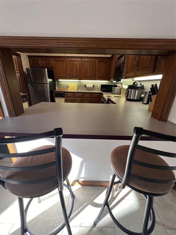 kitchen with freestanding refrigerator, black microwave, light countertops, and a peninsula