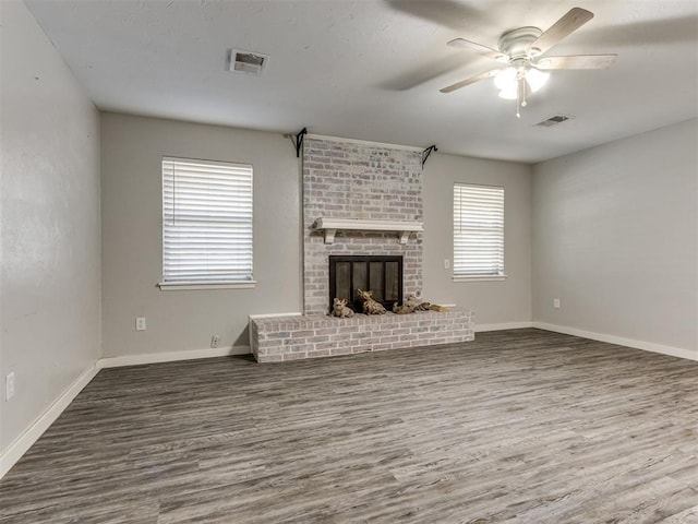 unfurnished living room with ceiling fan, a wealth of natural light, dark hardwood / wood-style flooring, and a brick fireplace