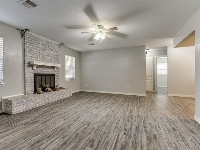 unfurnished living room with ceiling fan, plenty of natural light, a fireplace, and wood-type flooring