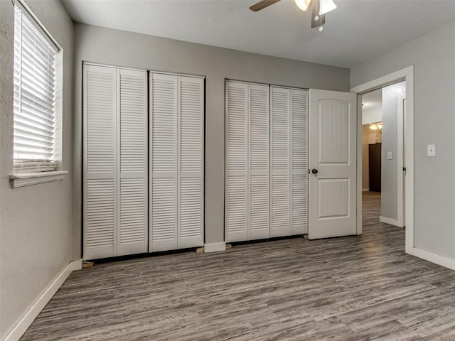 unfurnished bedroom with ceiling fan, hardwood / wood-style flooring, and multiple closets