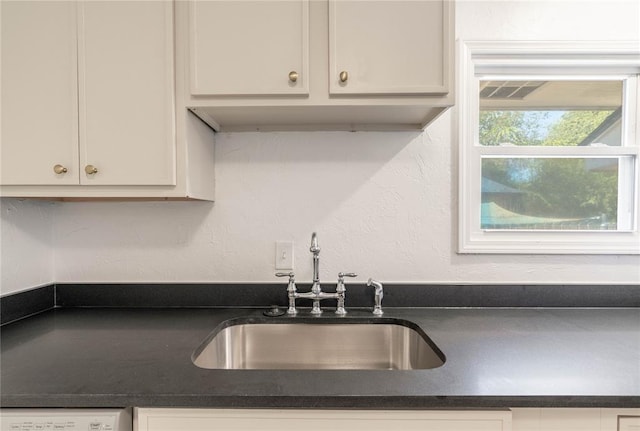 kitchen featuring white dishwasher, sink, and white cabinets