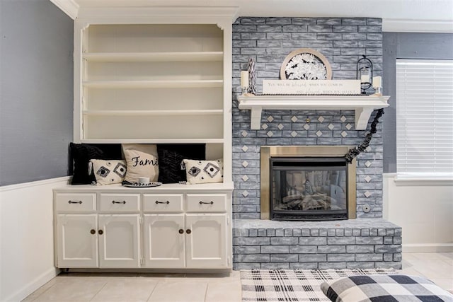 interior space featuring white cabinets, built in shelves, ornamental molding, a brick fireplace, and light tile patterned floors