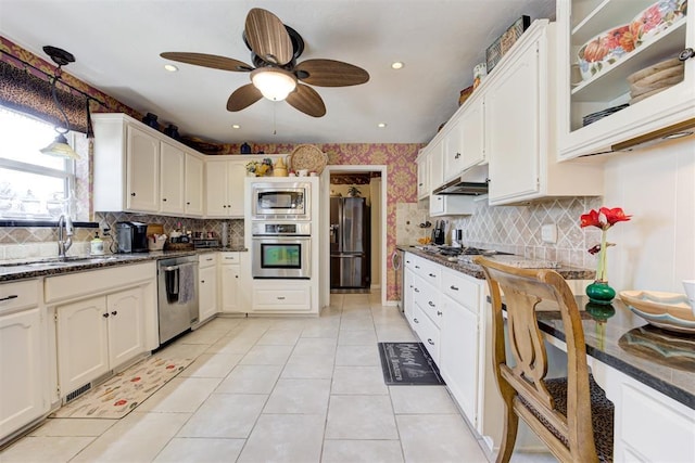 kitchen with ceiling fan, stainless steel appliances, light tile patterned flooring, dark stone countertops, and sink