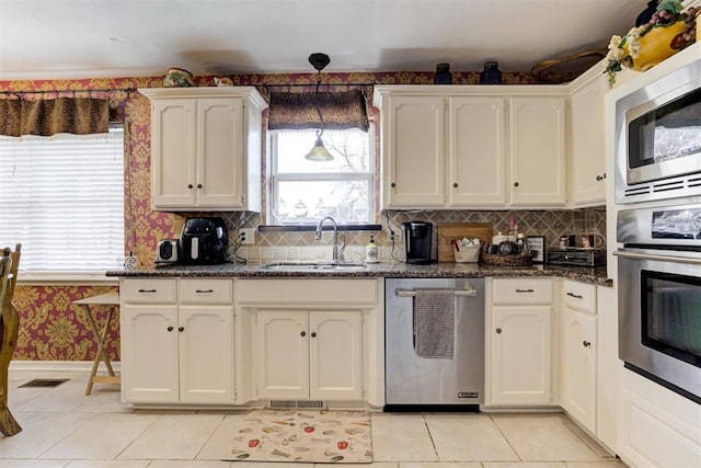 kitchen featuring sink, stainless steel appliances, dark stone counters, and light tile patterned flooring