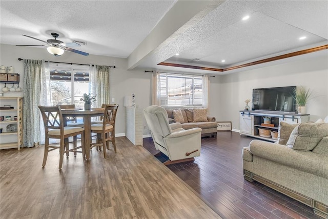 living room with dark hardwood / wood-style floors, ceiling fan, a tray ceiling, and a textured ceiling