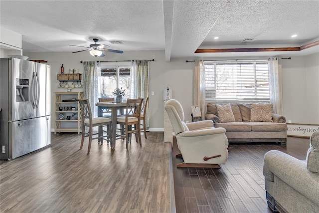 living room with dark hardwood / wood-style flooring, ceiling fan, a raised ceiling, and a textured ceiling