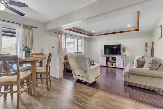 living room featuring a raised ceiling, dark hardwood / wood-style flooring, ceiling fan, and a textured ceiling