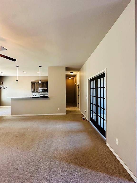 unfurnished living room featuring light carpet, ceiling fan with notable chandelier, and french doors