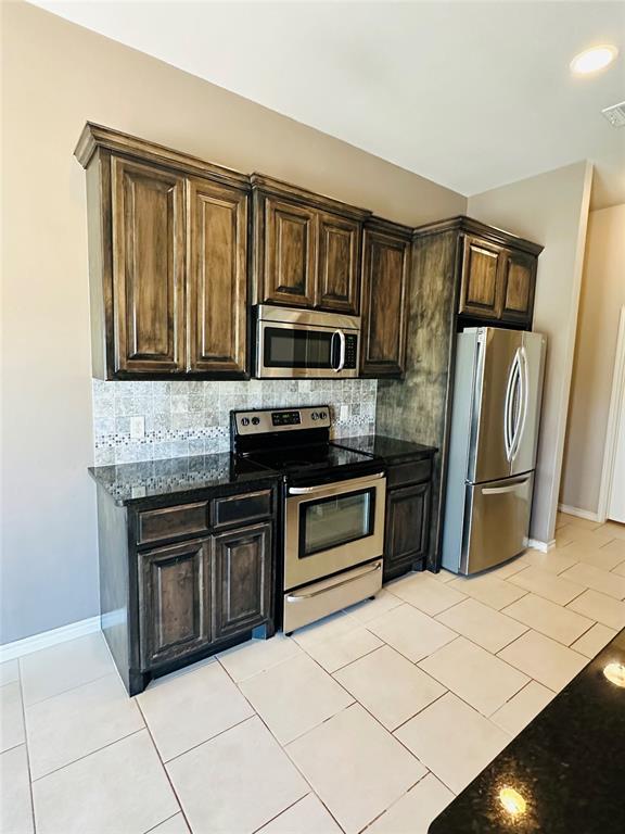 kitchen featuring decorative backsplash, light tile patterned flooring, dark brown cabinetry, appliances with stainless steel finishes, and dark stone counters