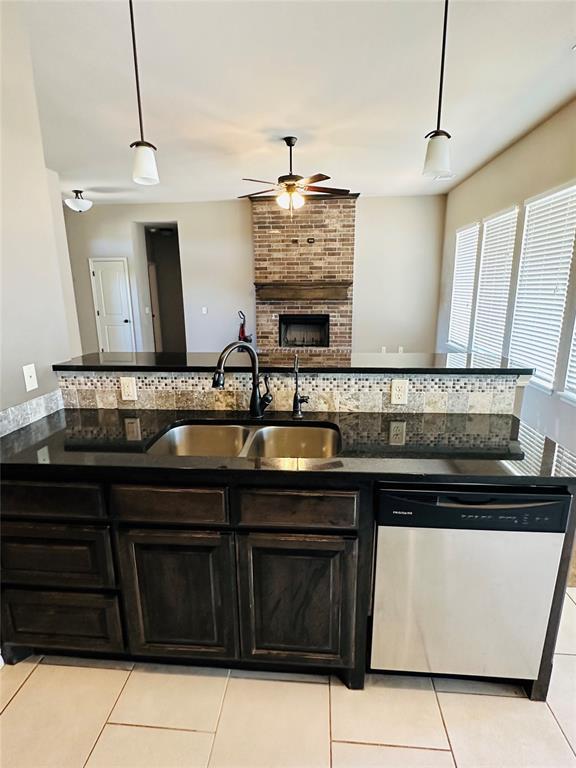 kitchen with light tile patterned floors, sink, hanging light fixtures, and stainless steel dishwasher