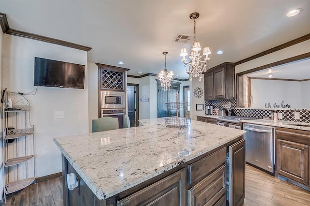 kitchen with hardwood / wood-style floors, appliances with stainless steel finishes, a chandelier, dark brown cabinetry, and a center island