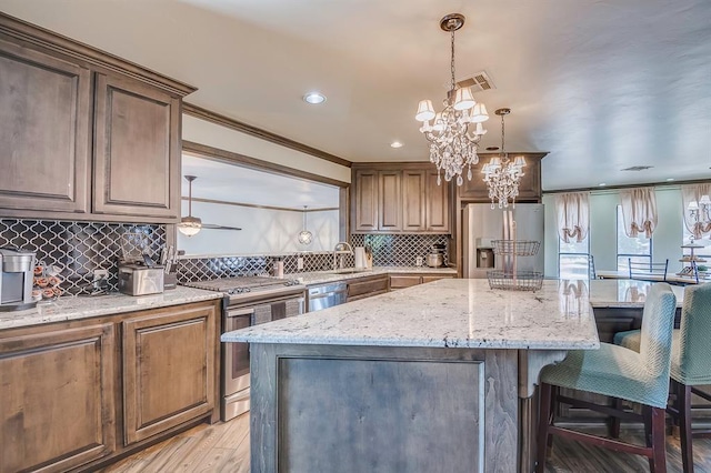 kitchen with a notable chandelier, a kitchen island, sink, appliances with stainless steel finishes, and light stone counters