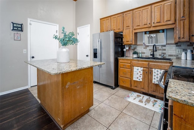 kitchen with stainless steel fridge with ice dispenser, light stone countertops, sink, and a center island